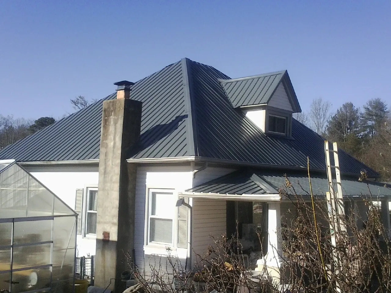 Dark blue standing seam metal roof on a white farmhouse with dormer — Slate & Tile Roof Repair by Roofing Brothers in Worthington Springs