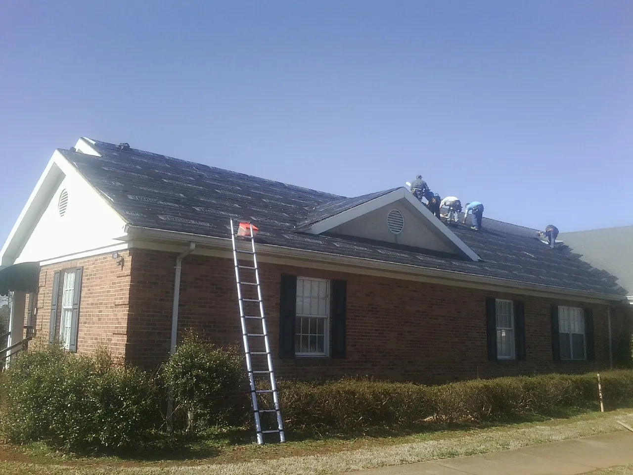 Crew tearing shingles off a brick ranch roof with a ladder set — Metal Roof Repair work by our crew in Worthington Springs