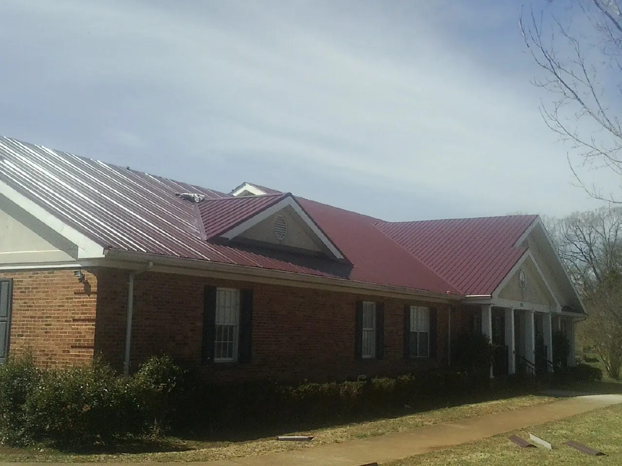 Red metal roof with gabled entries on a long brick building, from a Hail Damage Roof Repair job in Worthington Springs