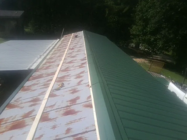 Old rusted panels beside newly installed green metal roofing — Wind Damage Roof Repair by Roofing Brothers in Worthington Springs