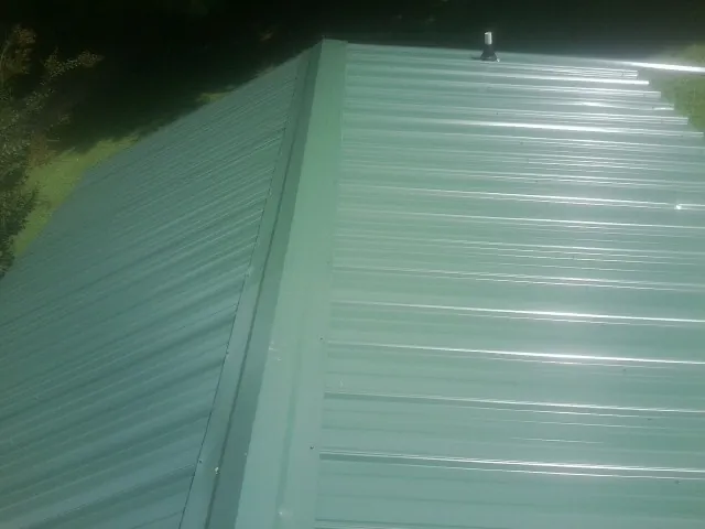 New green metal panels meeting at the ridge of a roof — Flat Roof Repair work by our crew in Worthington Springs