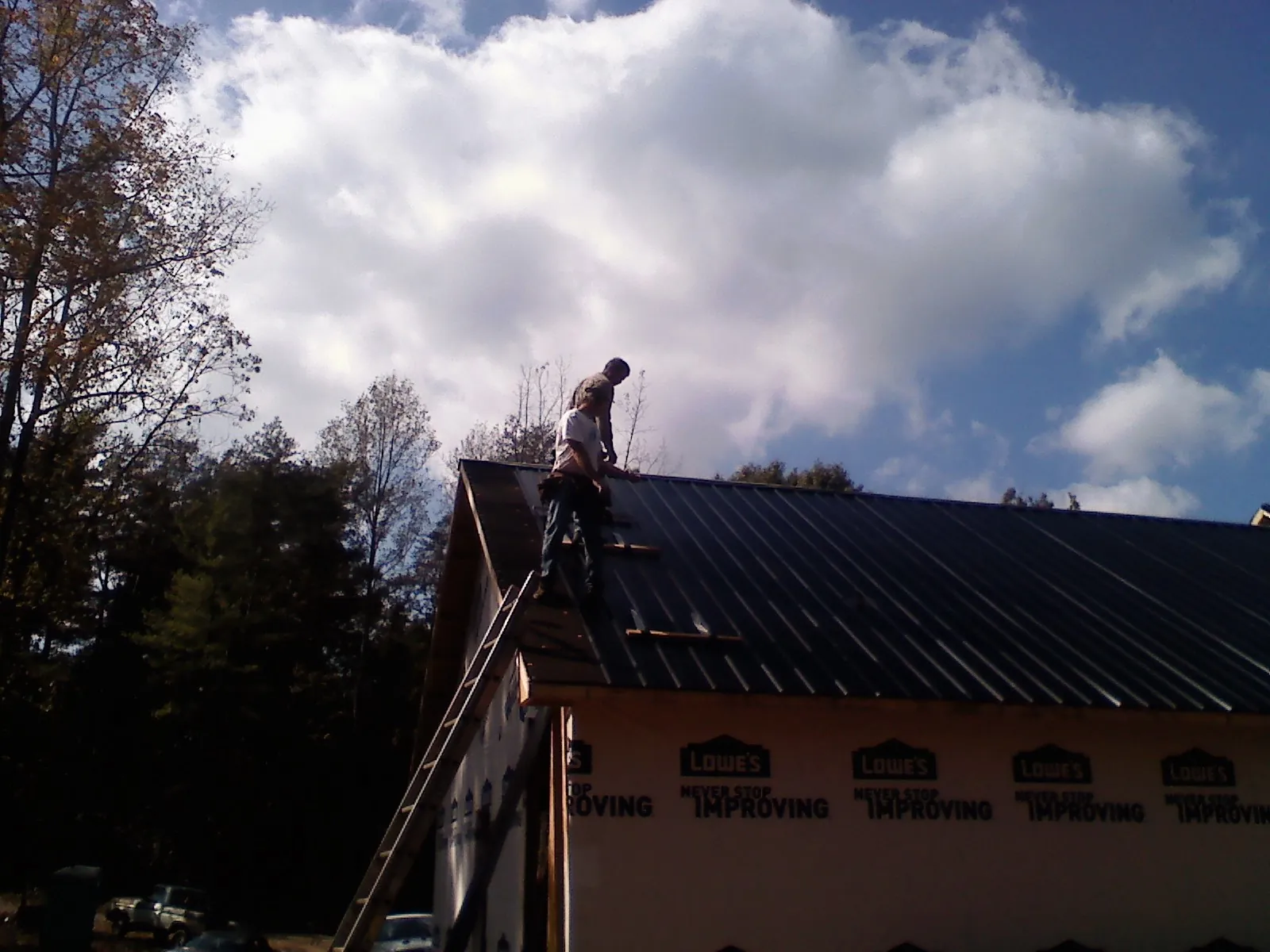 Roofer fastening dark metal panels high against a cloudy sky, from a Roof Inspection job in Worthington Springs