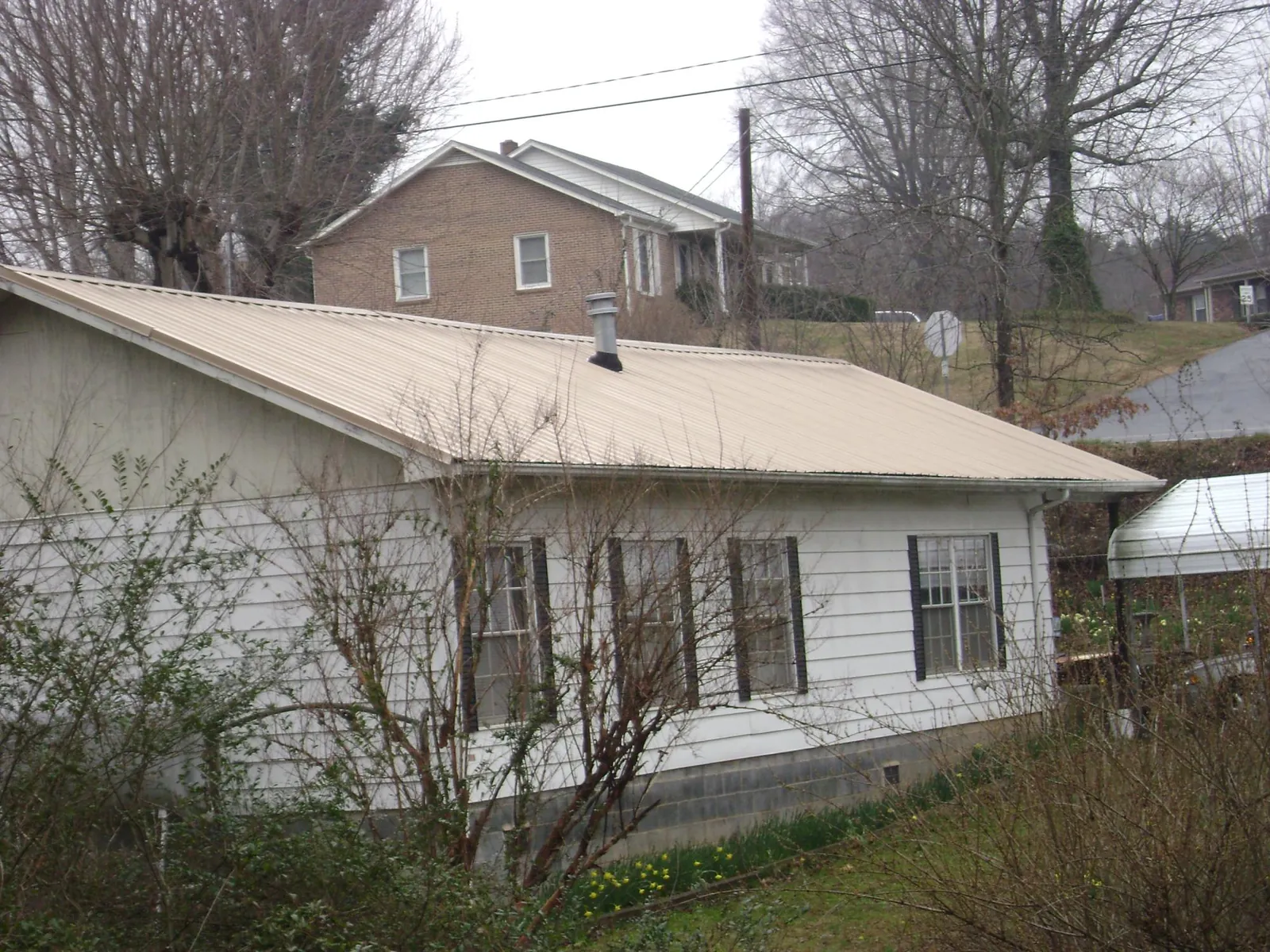 Tan metal roof on a white sided house set into a hillside — Commercial Roofing by Roofing Brothers in Worthington Springs