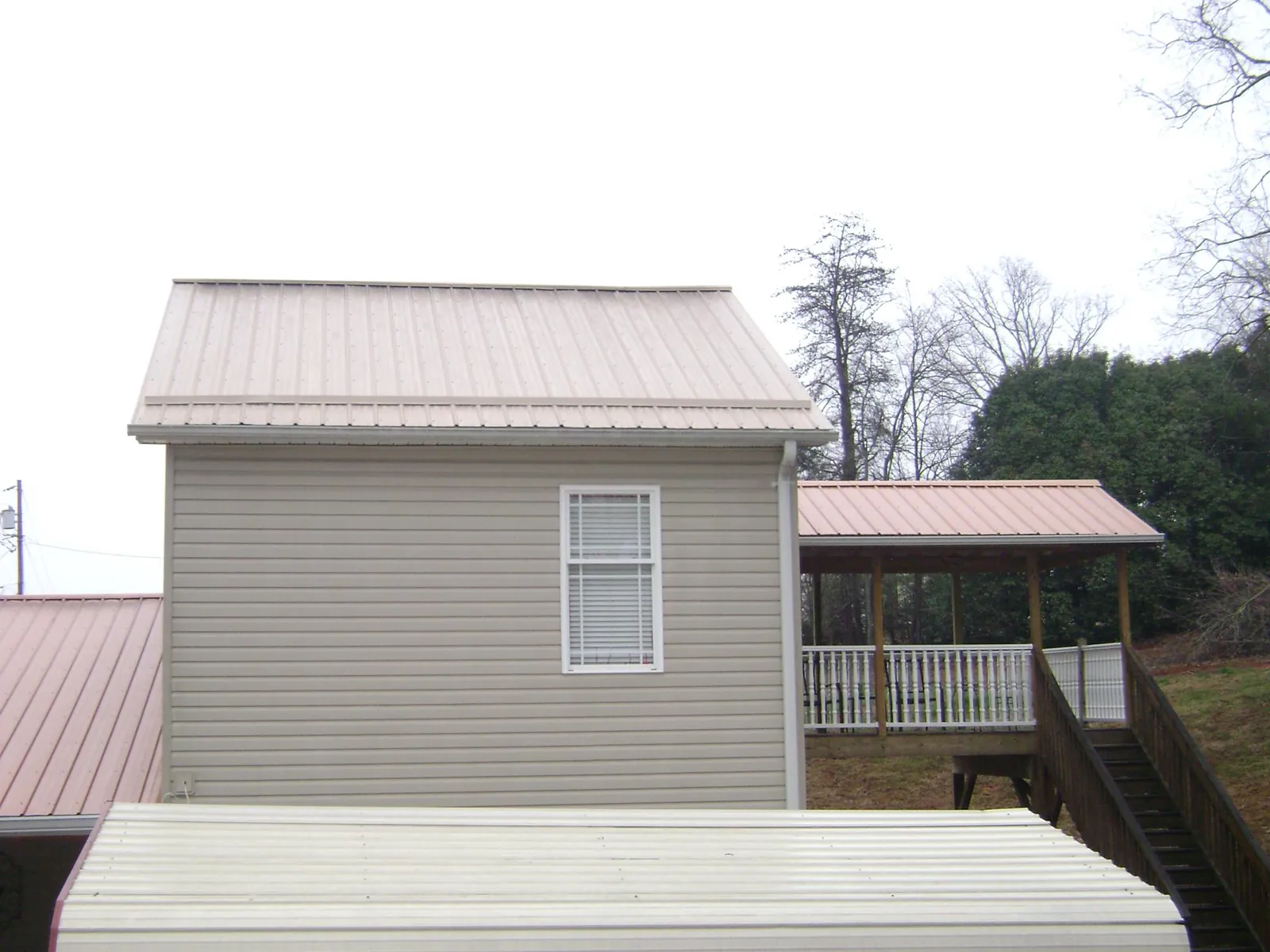 Tan metal roofs on a two story addition and attached porch, from a Roof Replacement job in Worthington Springs